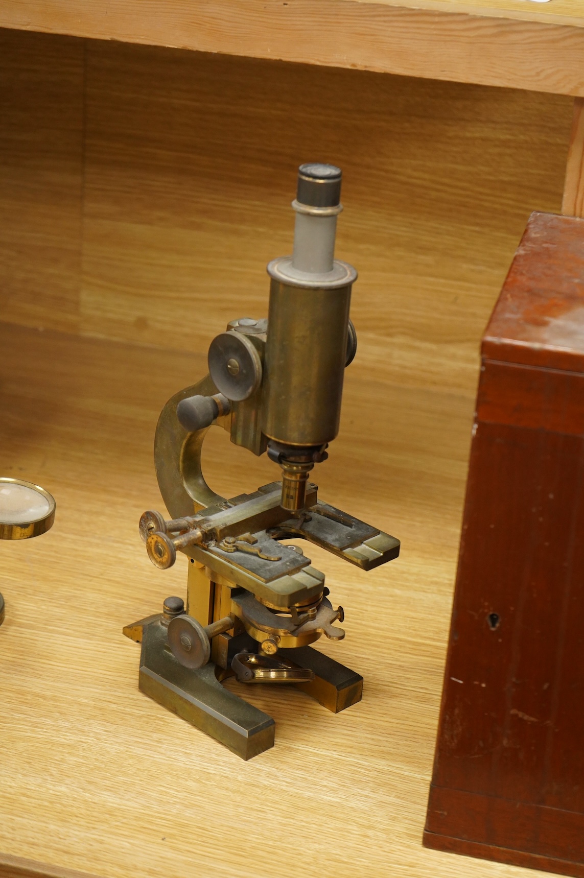 An early 20th century brass compound monocular microscope, by R & J Beck, Ltd., London, number 33007, with accessories including spare lenses, a free standing magnifier and objectives, mahogany cased; 34.5cm high, 19cm w